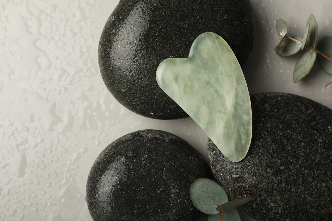 Jade Gua Sha Tool, Spa Stones and Eucalyptus Branches on Grey Ta